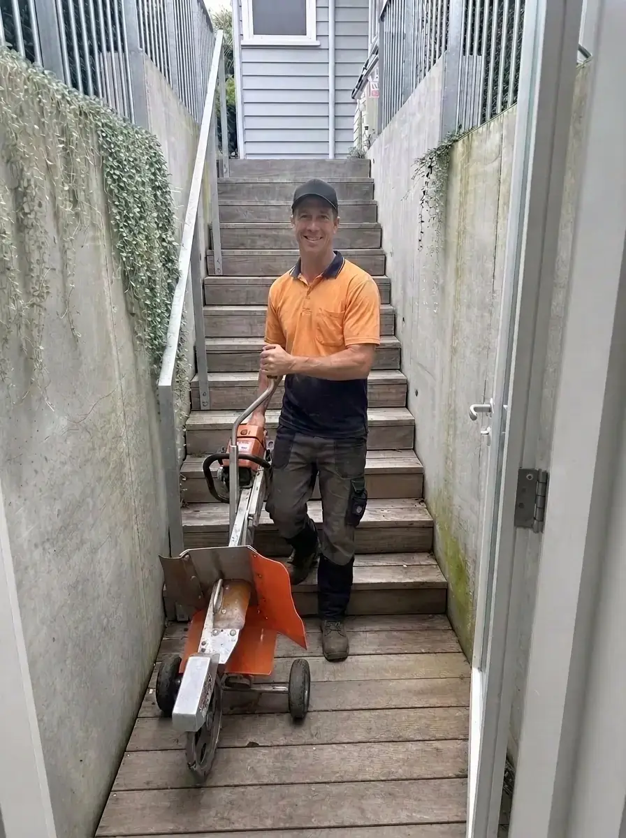 Portable stump grinder being carried down narrow outdoor stairs to reach a stump